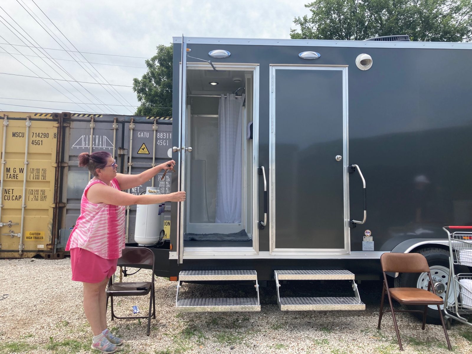 Dena Lantz, the director of the Connecting Grounds Outreach Center, hold open a door to one of three shower stalls on the new shower trailer.