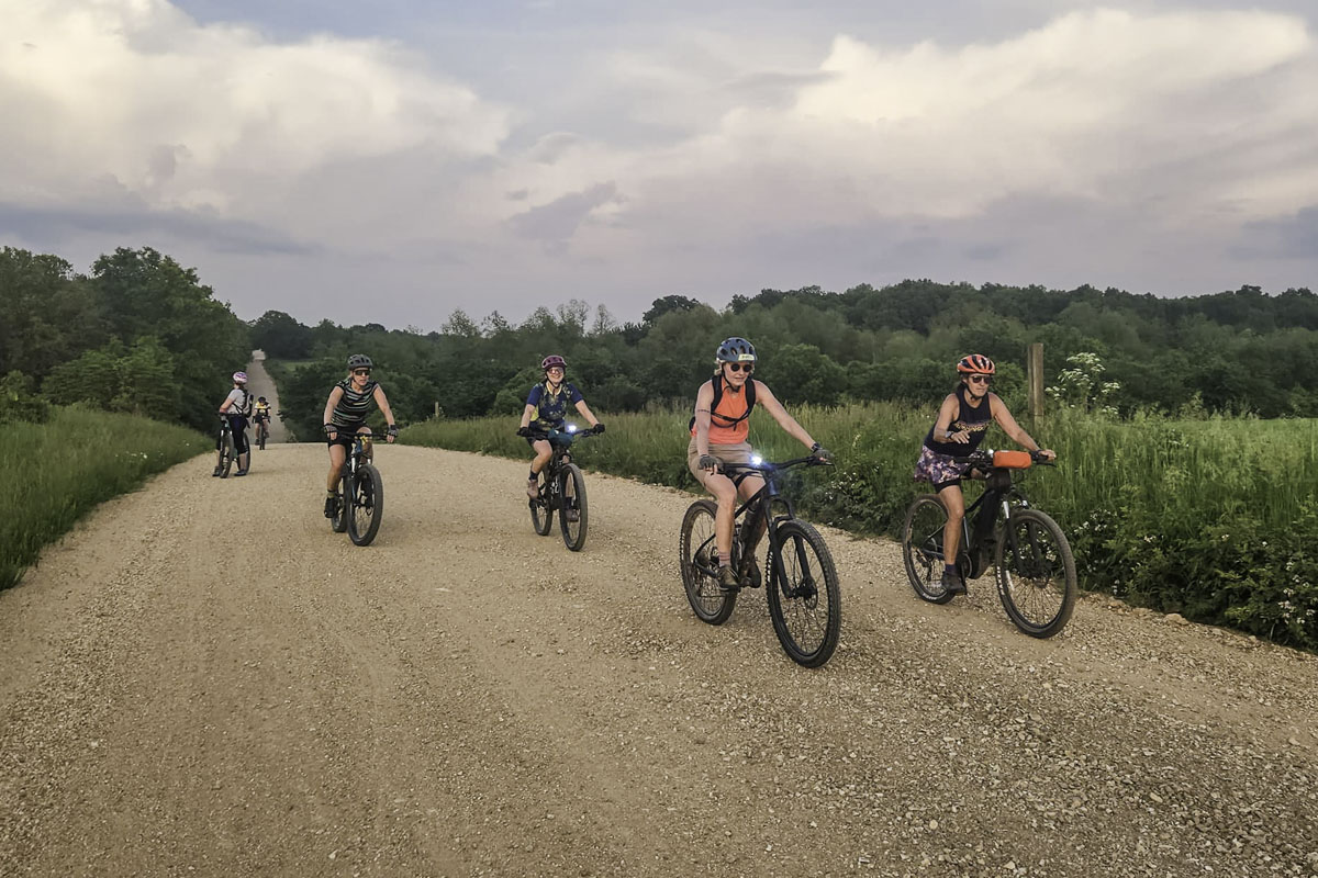 A group of 6 women ride their bikes down a gravel road out in the country
