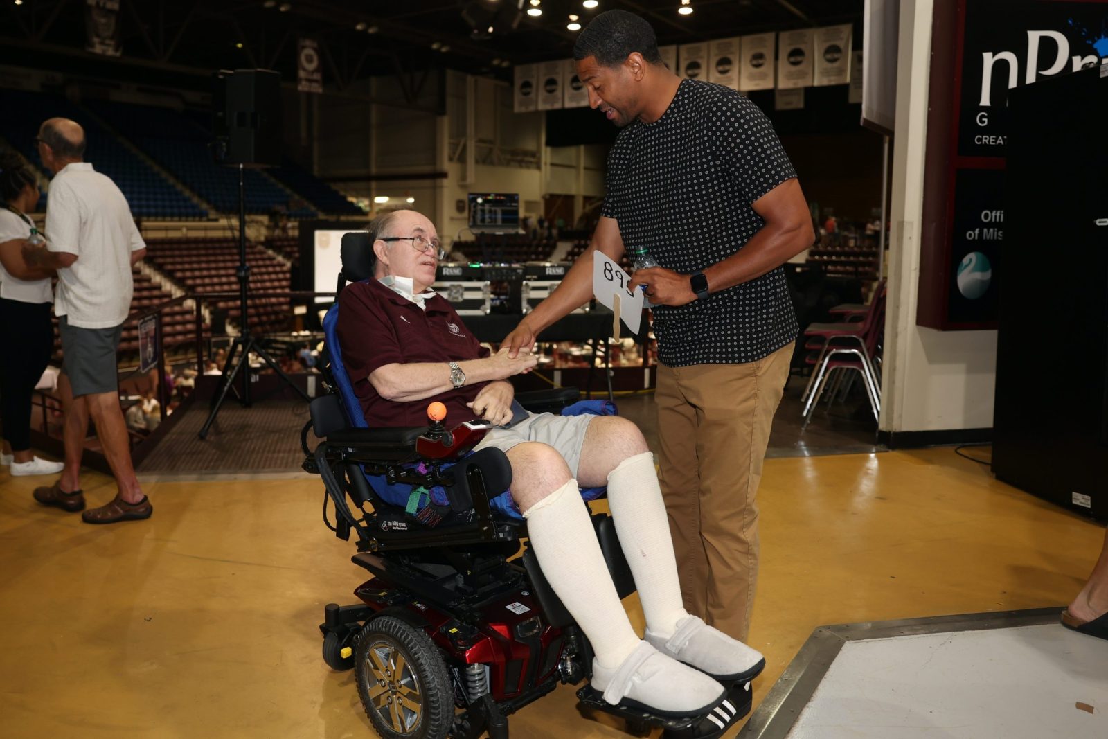 Art Hains, wearing a maroon shirt, sits in his wheelchair talking to Missouri State Bears basketball coach Dana Ford.