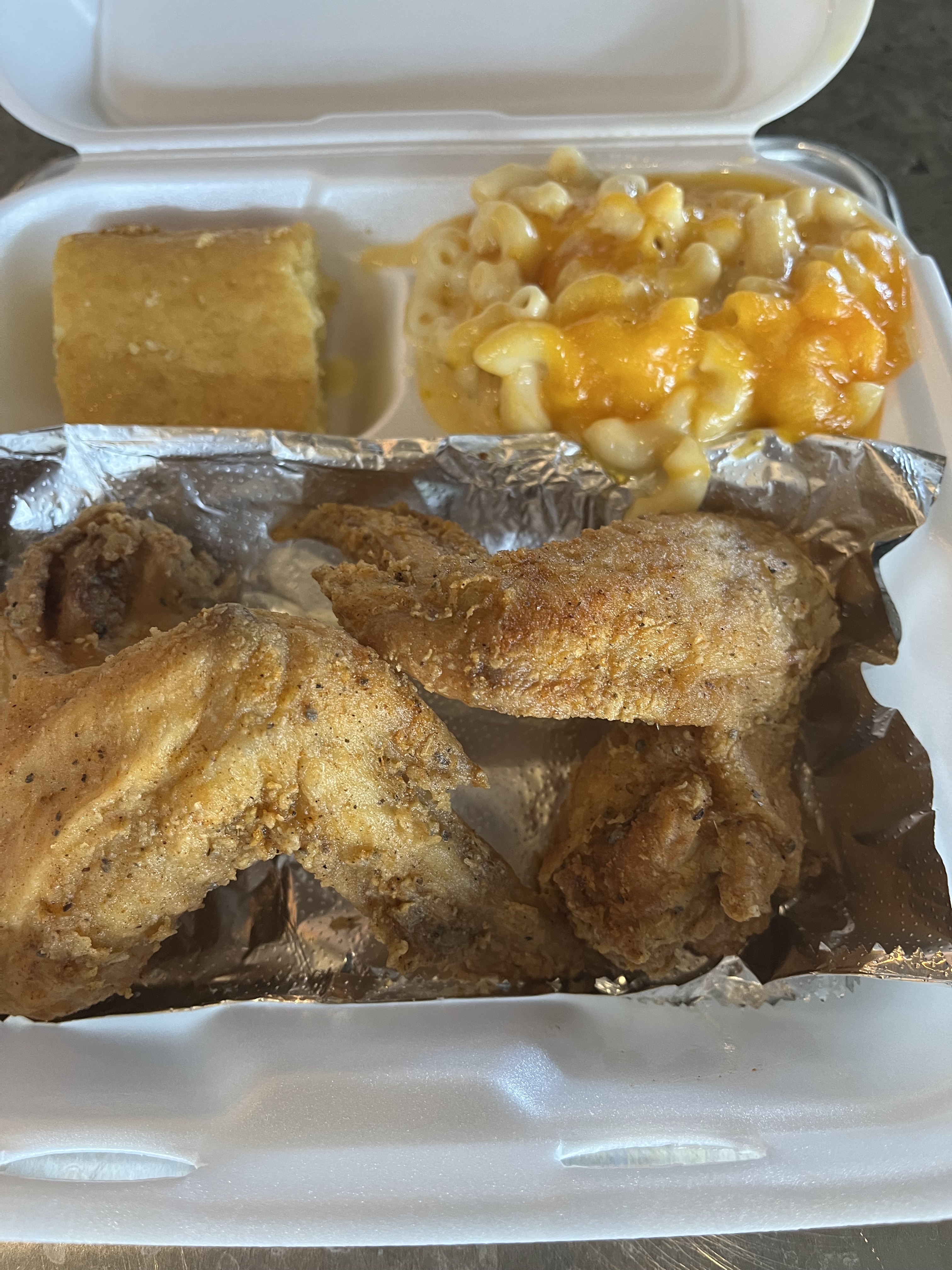 A Styrofoam food container holding fried chicken, mac-and-cheese and a piece of cornbread