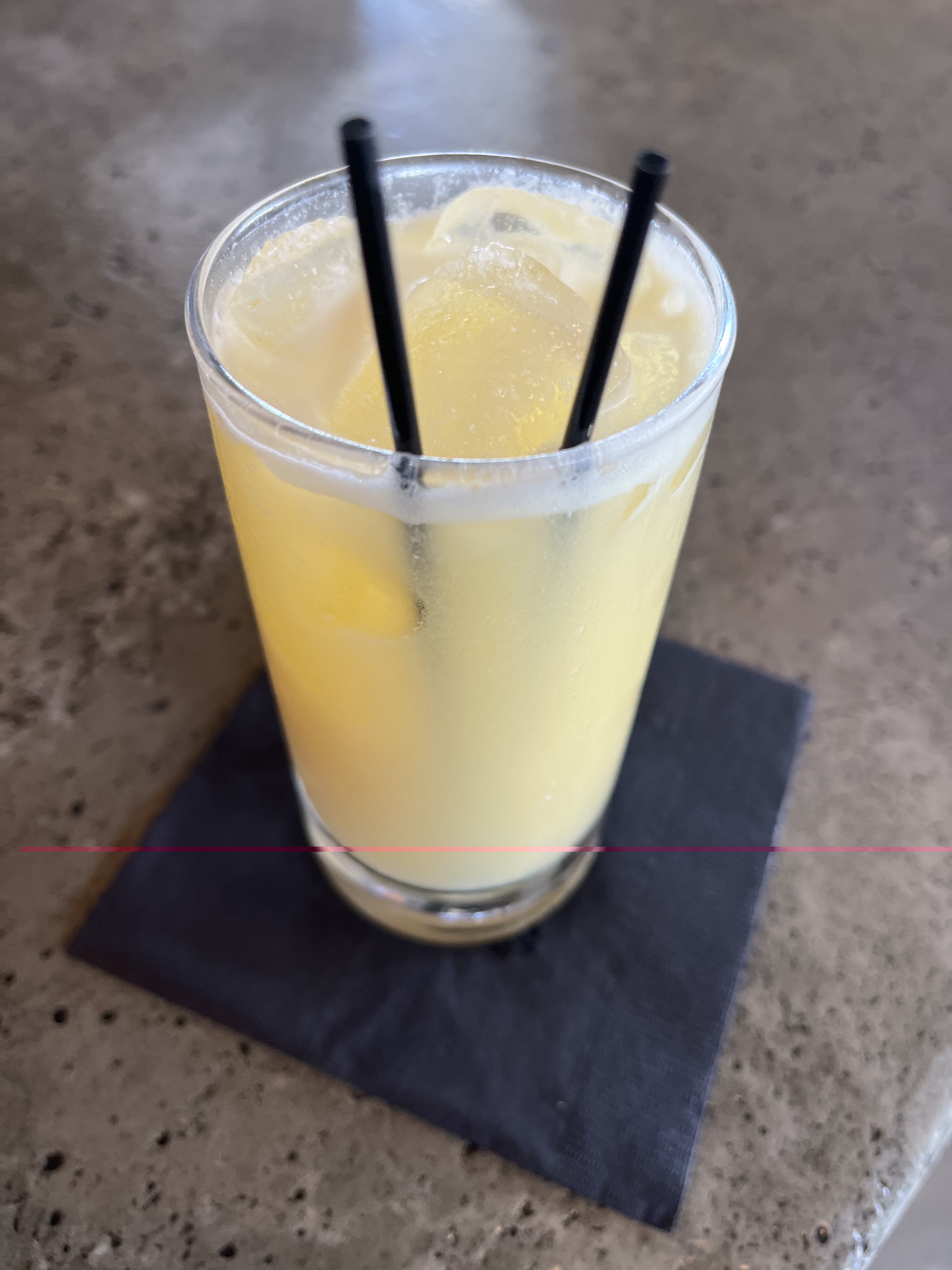 A yellow cocktail in a pint glass sits on a black napkin