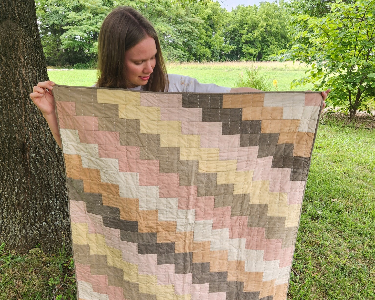 A woman stands next to a tree, holding a quilt