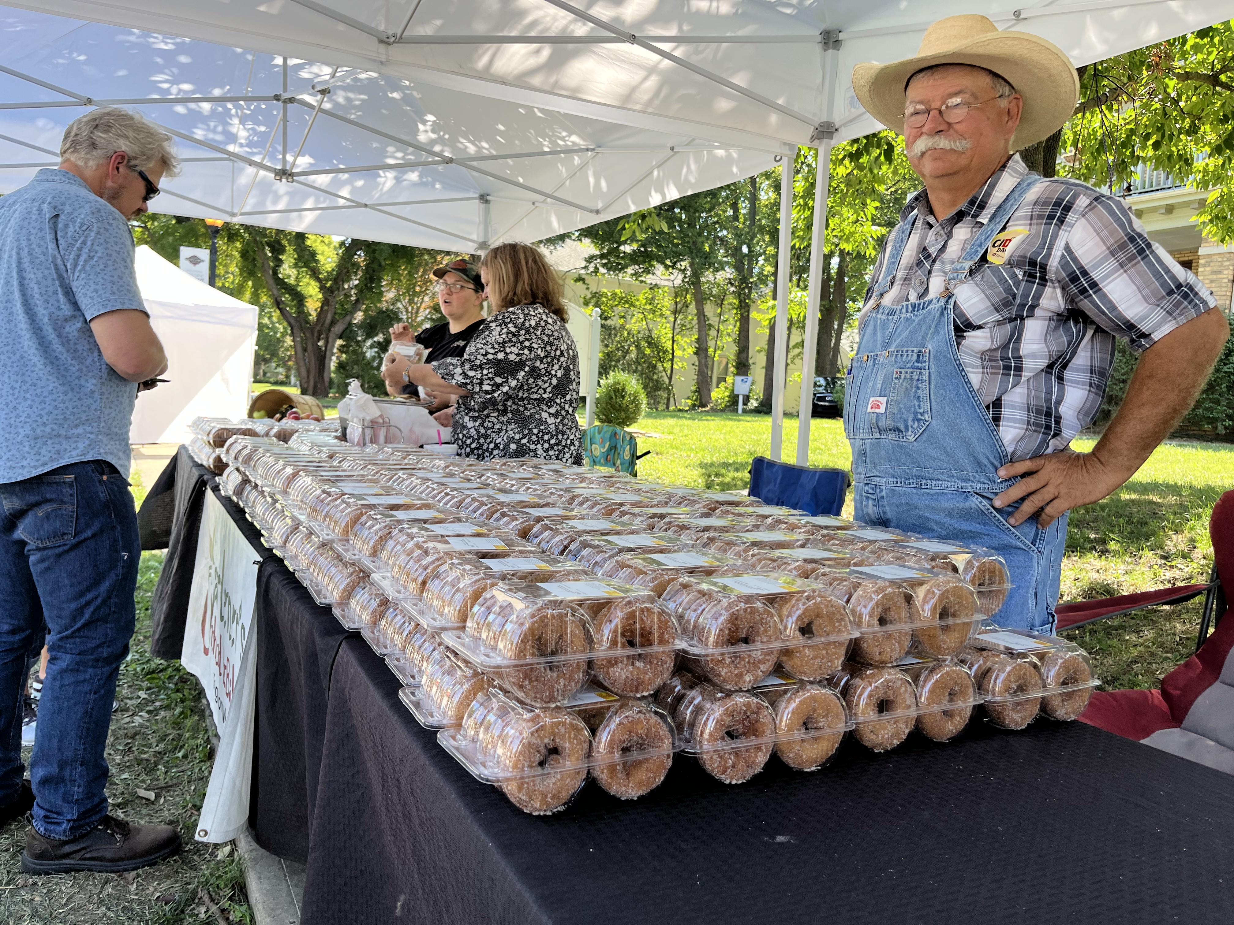 A man stands behind a table holding containers of apple cider donuts