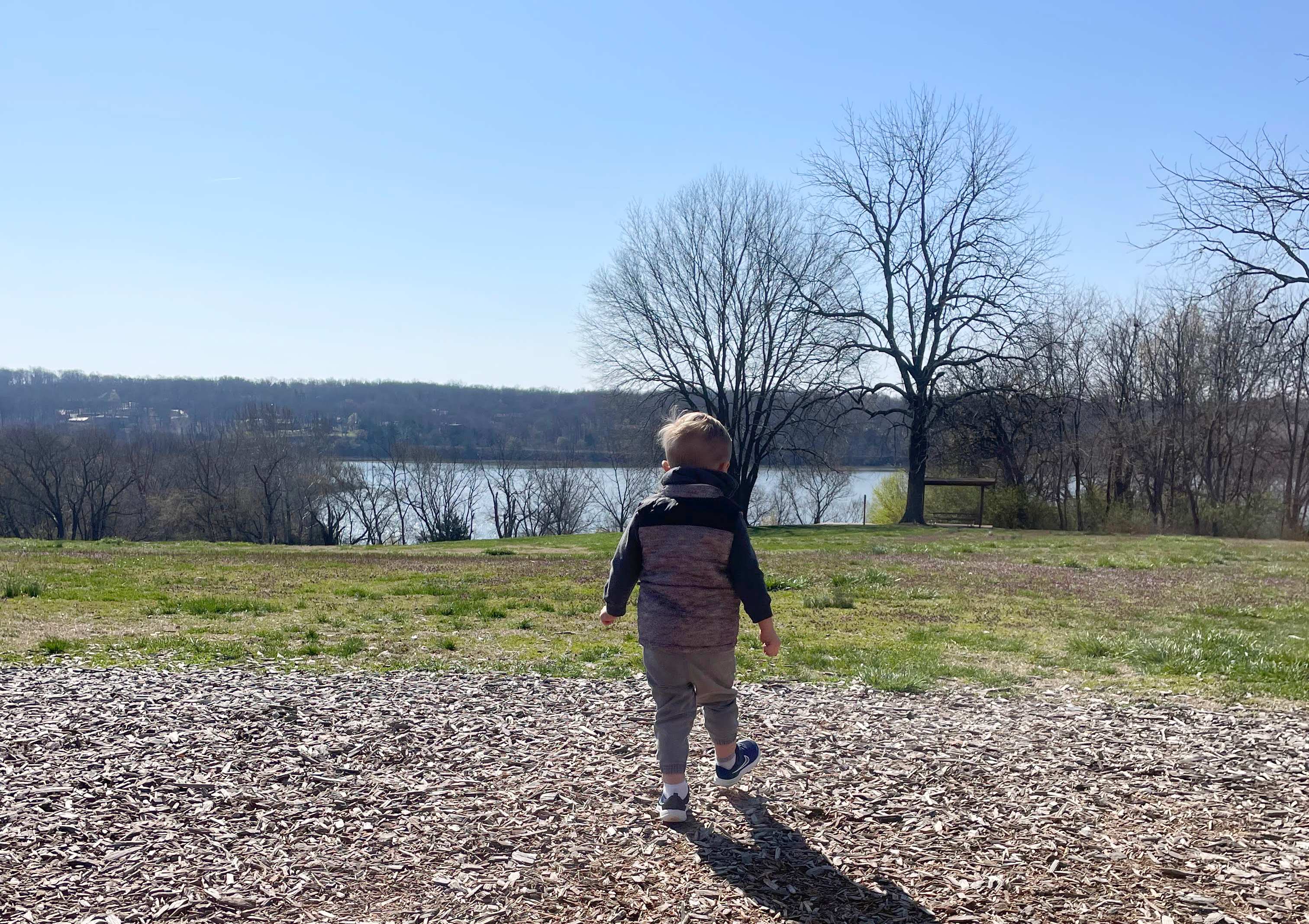 A child walks away from the playground at Lake Springfield Park toward the grassy hill overlooking the lake.