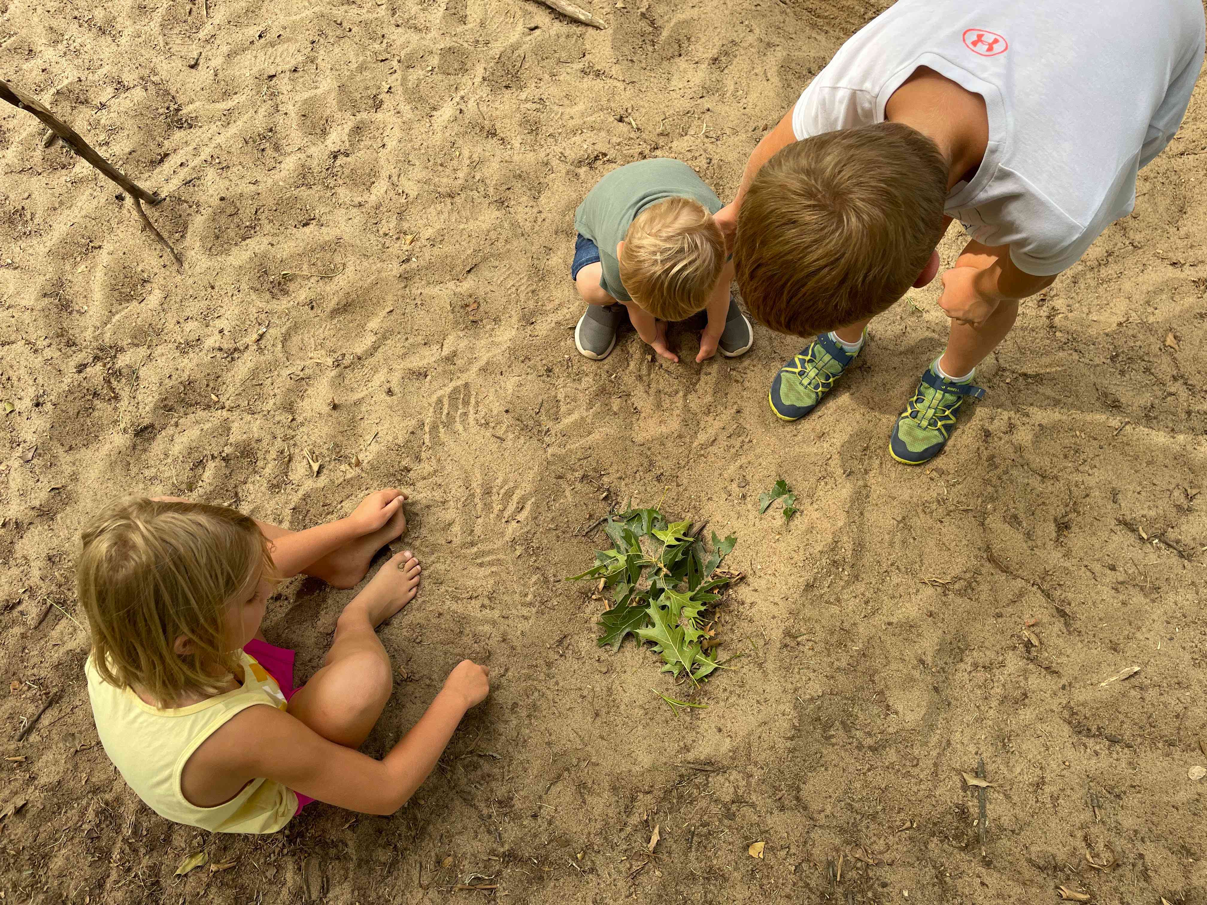 Children dig a shallow hole and fill it with leaves in sticks in a pretend game of “cooking soup.”