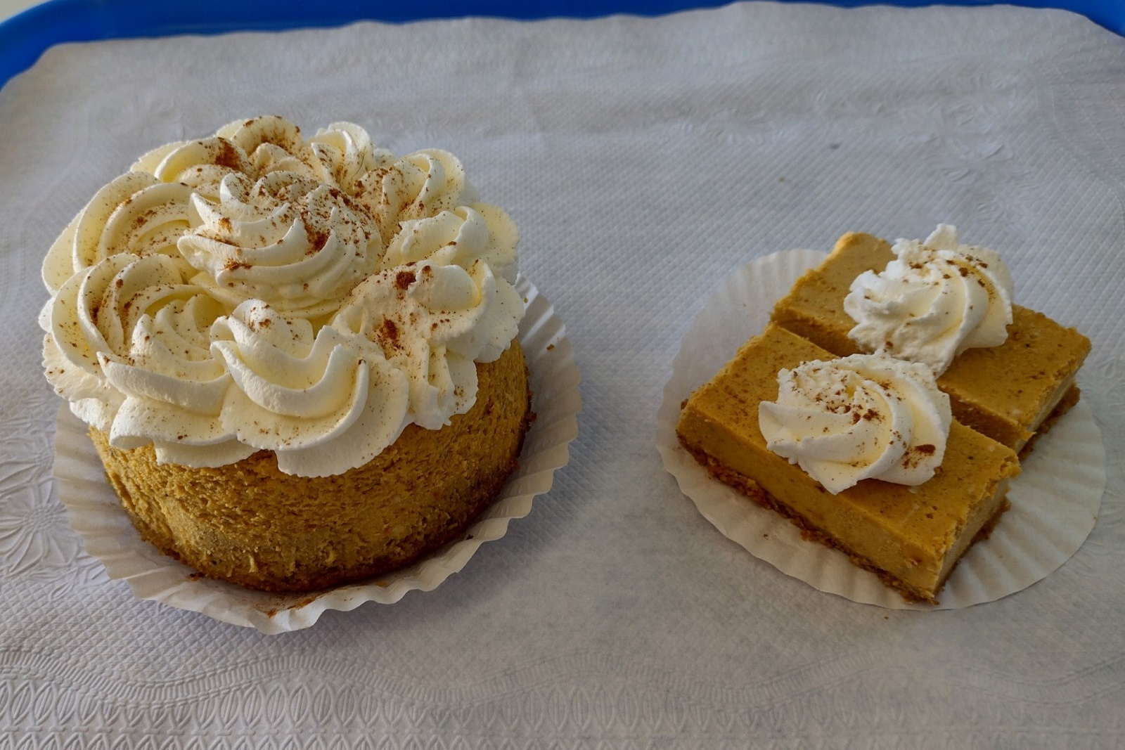 A small pumpkin cheesecake sits on a tray next to two bite-sized pieces