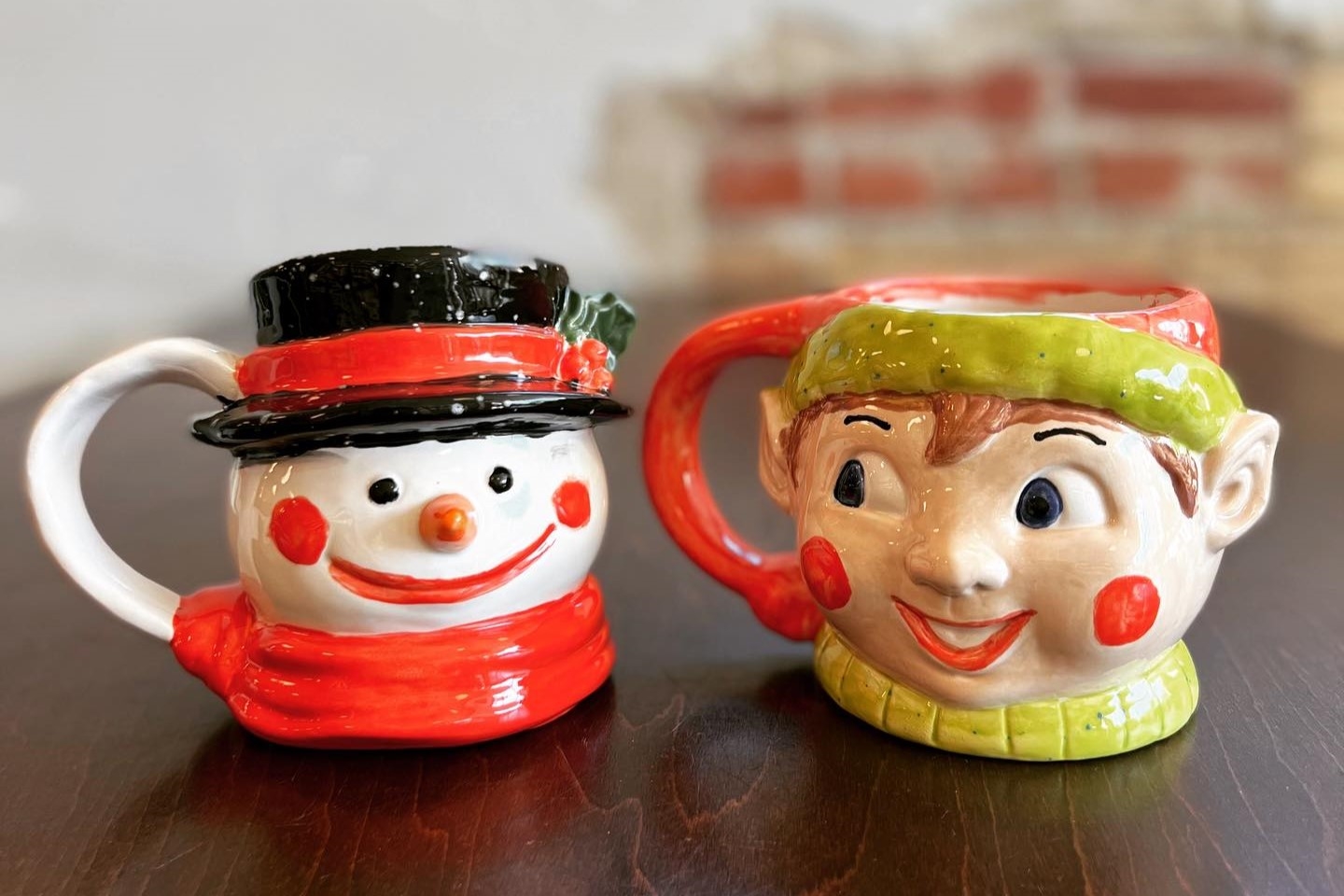 A snowman mug sits on a table next to an elf mug