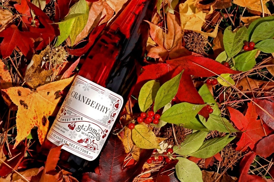A bottle of St. James Cranberry wine rests on a bed of fall leaves