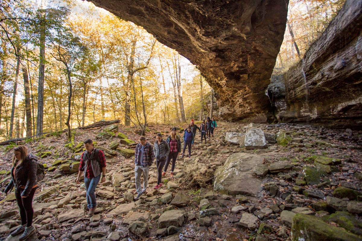 A group of hikers on a rocky trail, underneath a natural bridge.