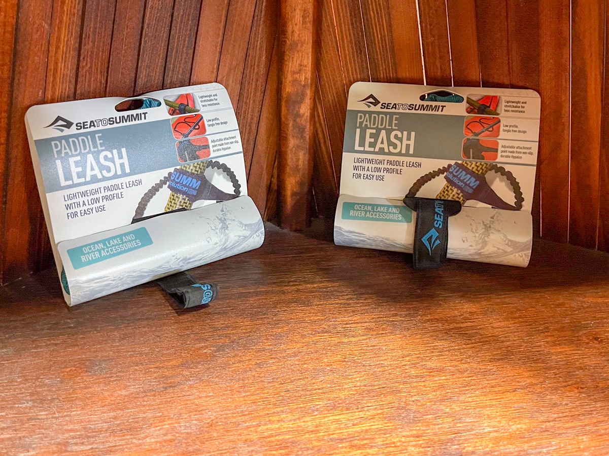 Two paddle leashes, in their packaging, sit on a wooden shelf.