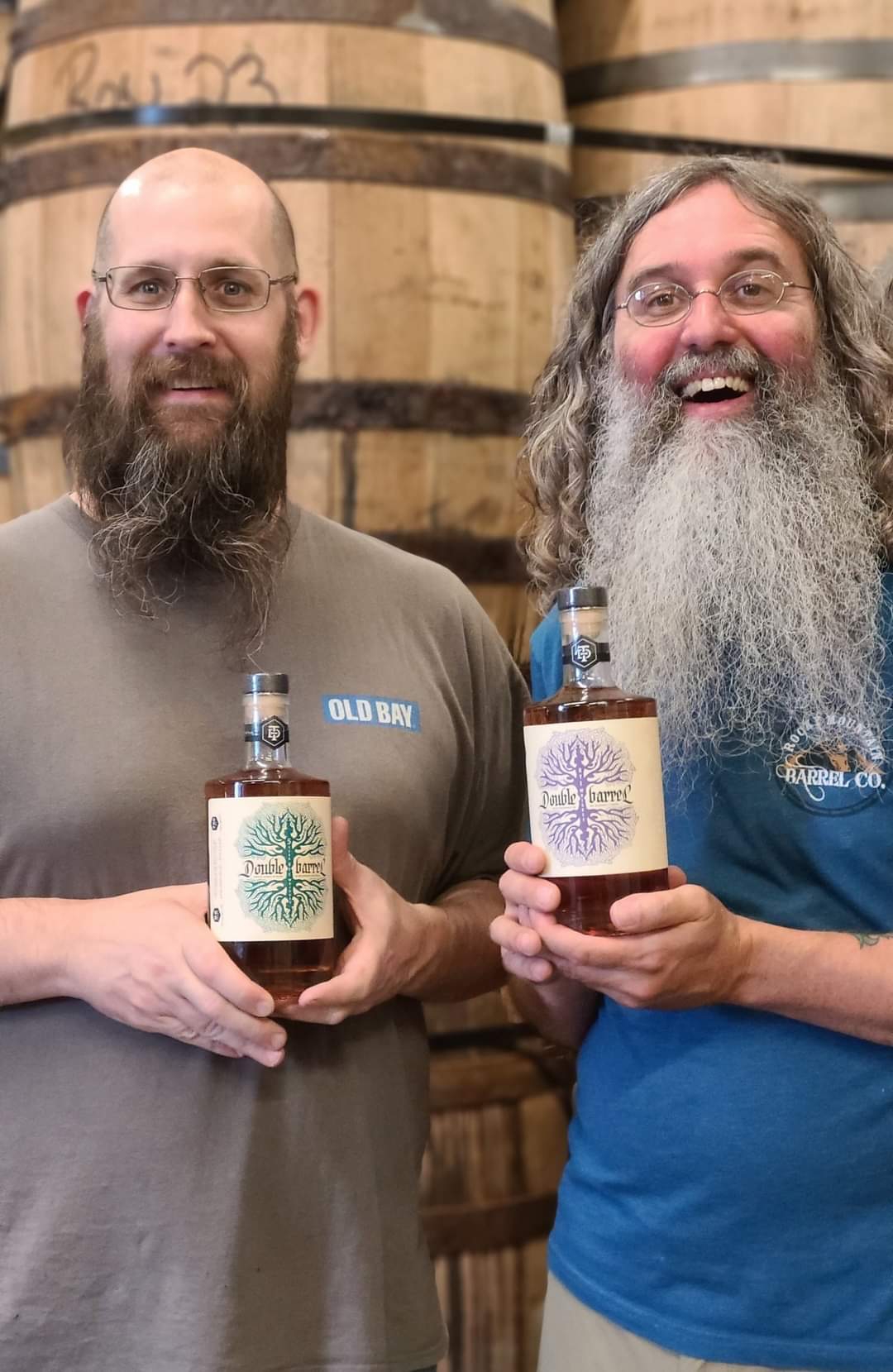 Andrew "Skippy" Steiger, left, and Brandon Moore hold bottles of Ty Iechyd Da spirits as they stand in the distillery's barrel room.