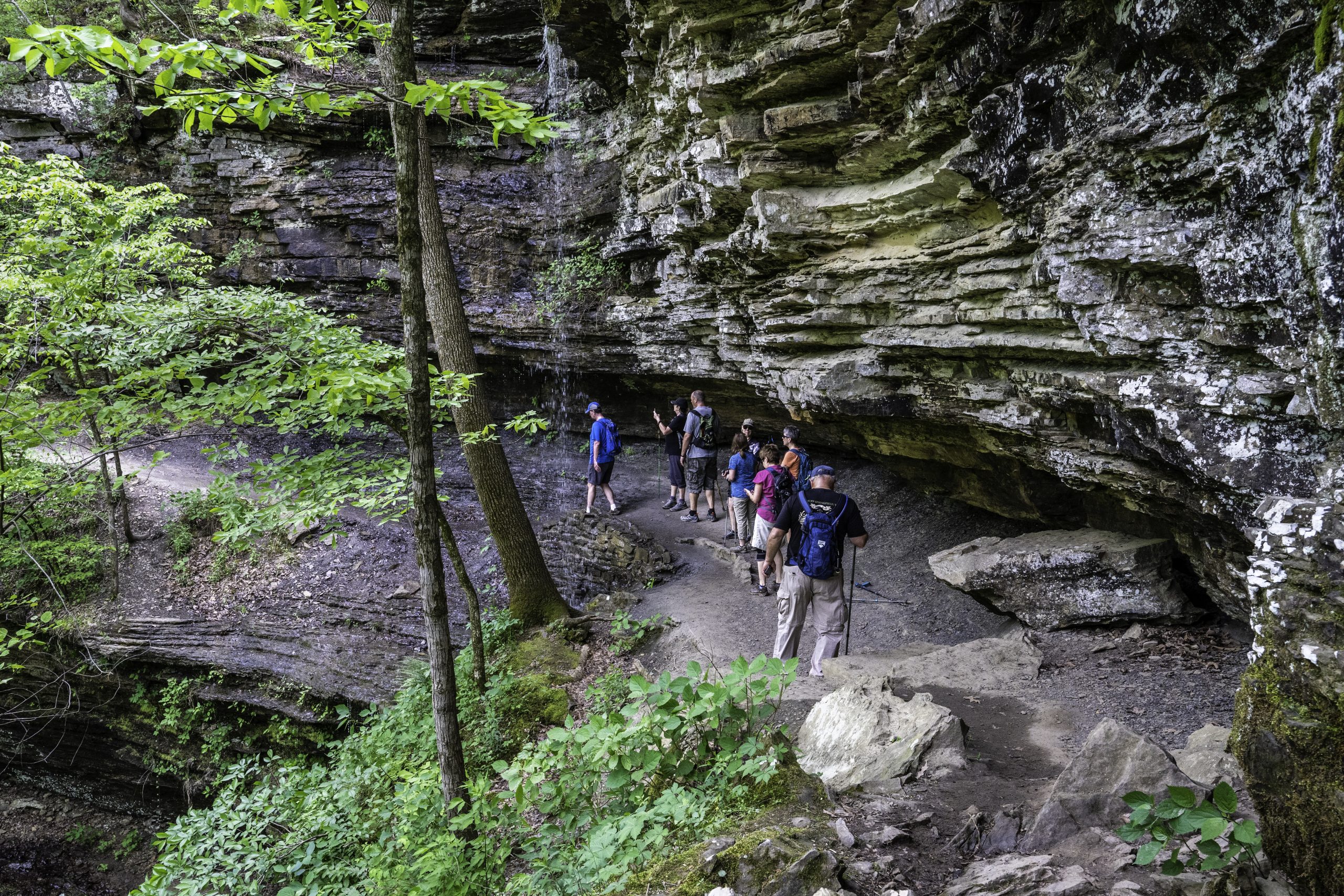 Hikers walk behind a waterfall on a trail at Devil’s Den State Park. (Photo by Sony Hocklander)