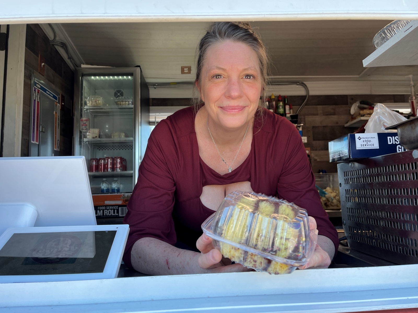 Stephanie Wigger, wearing a red shirt and holding a slice of cake in a plastic container, leans out of the window of The Gypsy food truck.