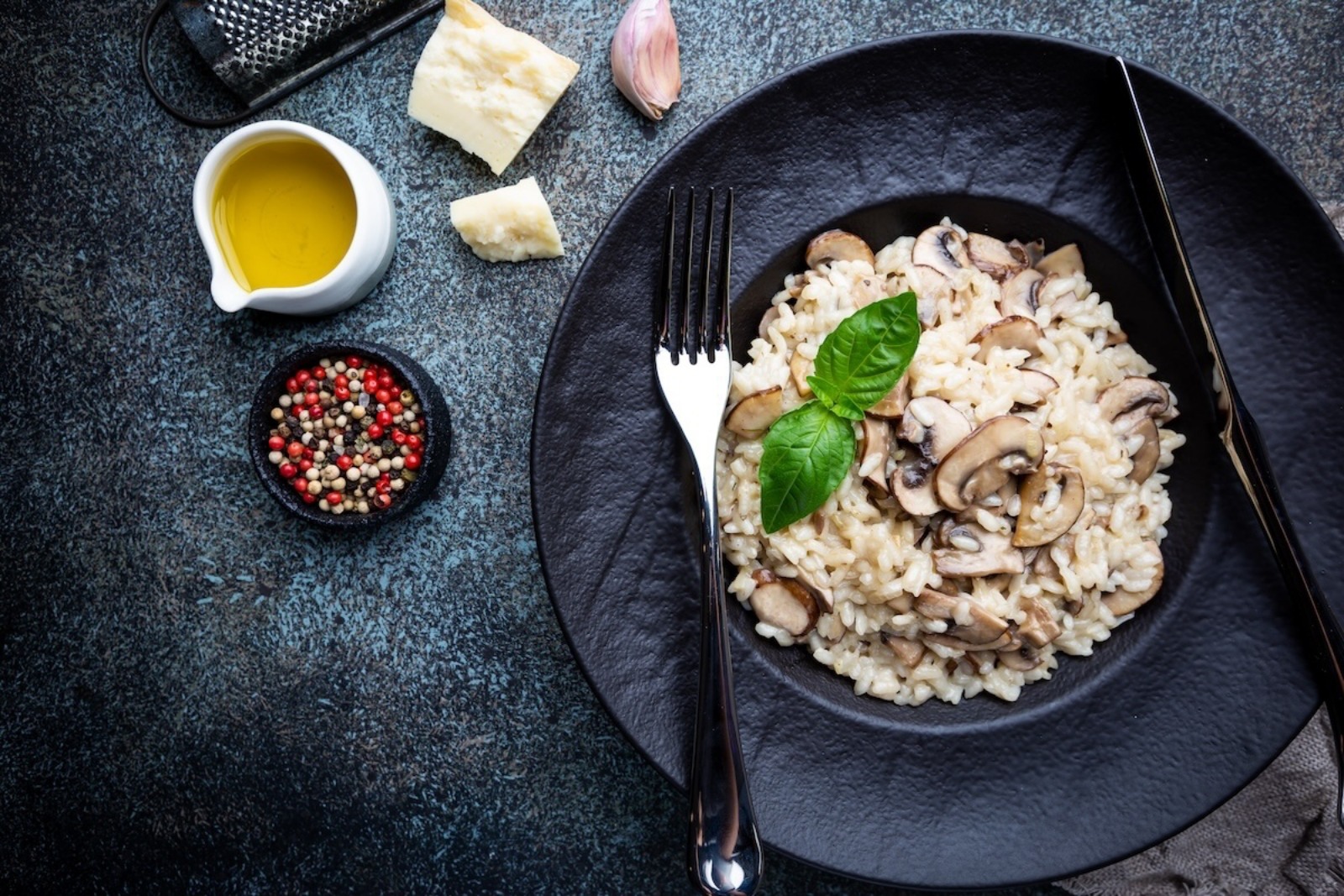 Risotto with mushrooms in a black plate over dark background, top view