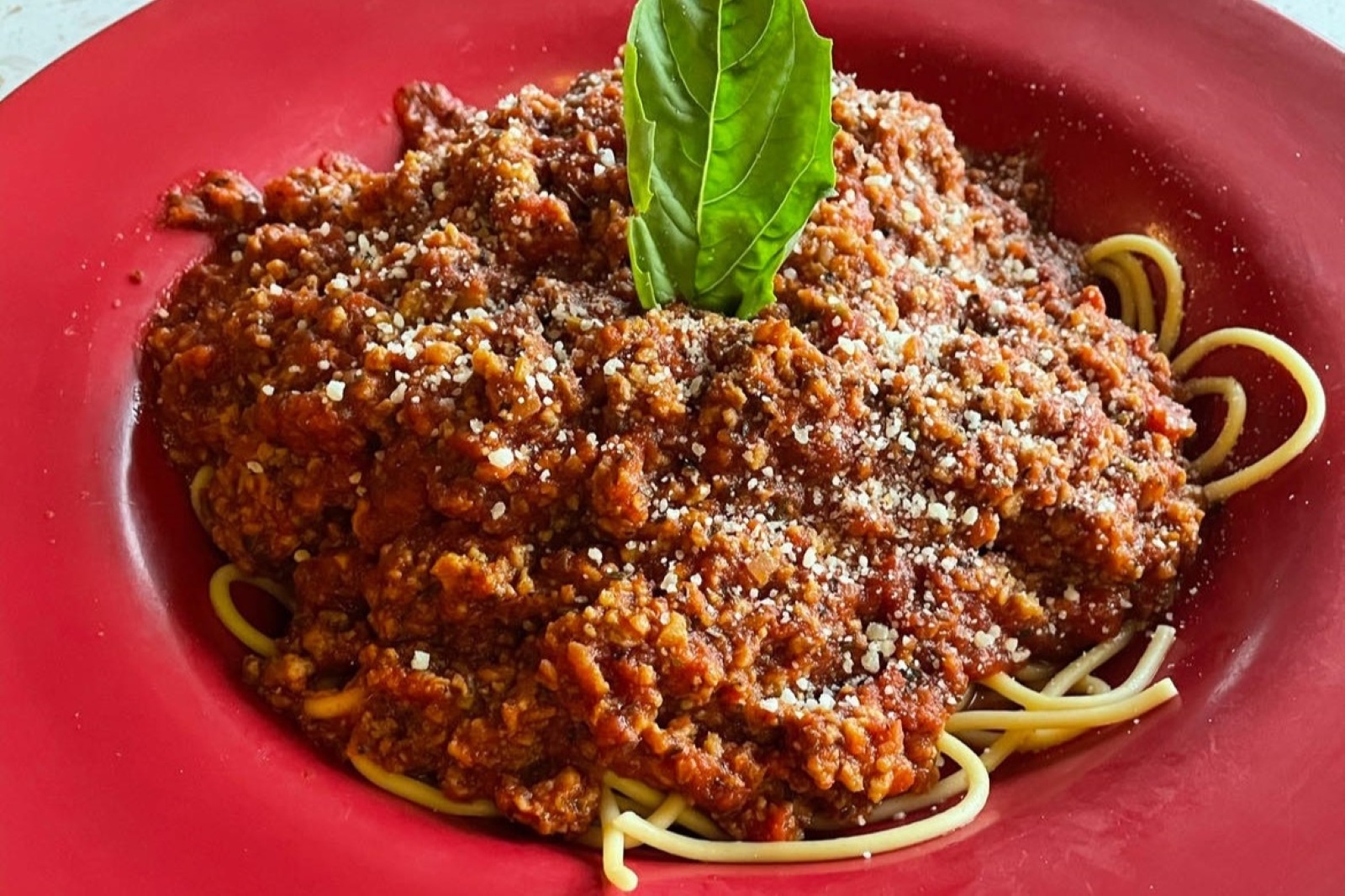A spaghetti dish from Piccolo, featuring Jake's Vegan crumbles, on a red plate.