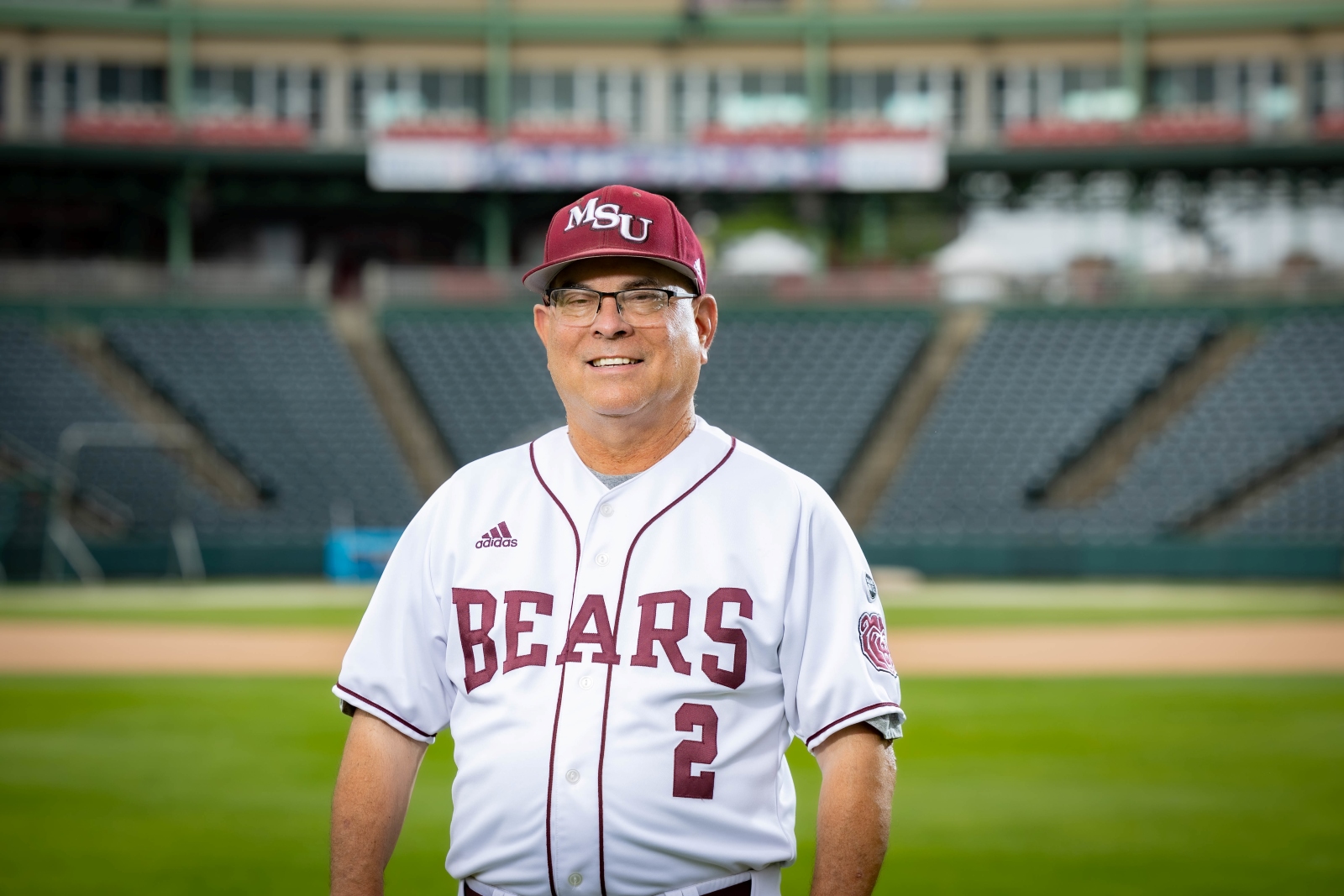 Missouri State baseball coach Keith Guttin, wearing a Bears uniform, poses for a picture on the outfield at Hammons Field