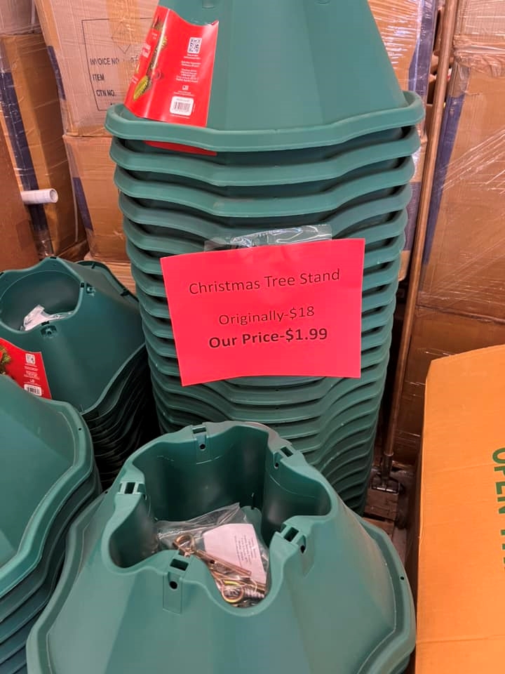 Green Christmas tree stands with a red sign reading, "Christmas tree stand. Originally - $18 Our price - $1.99"