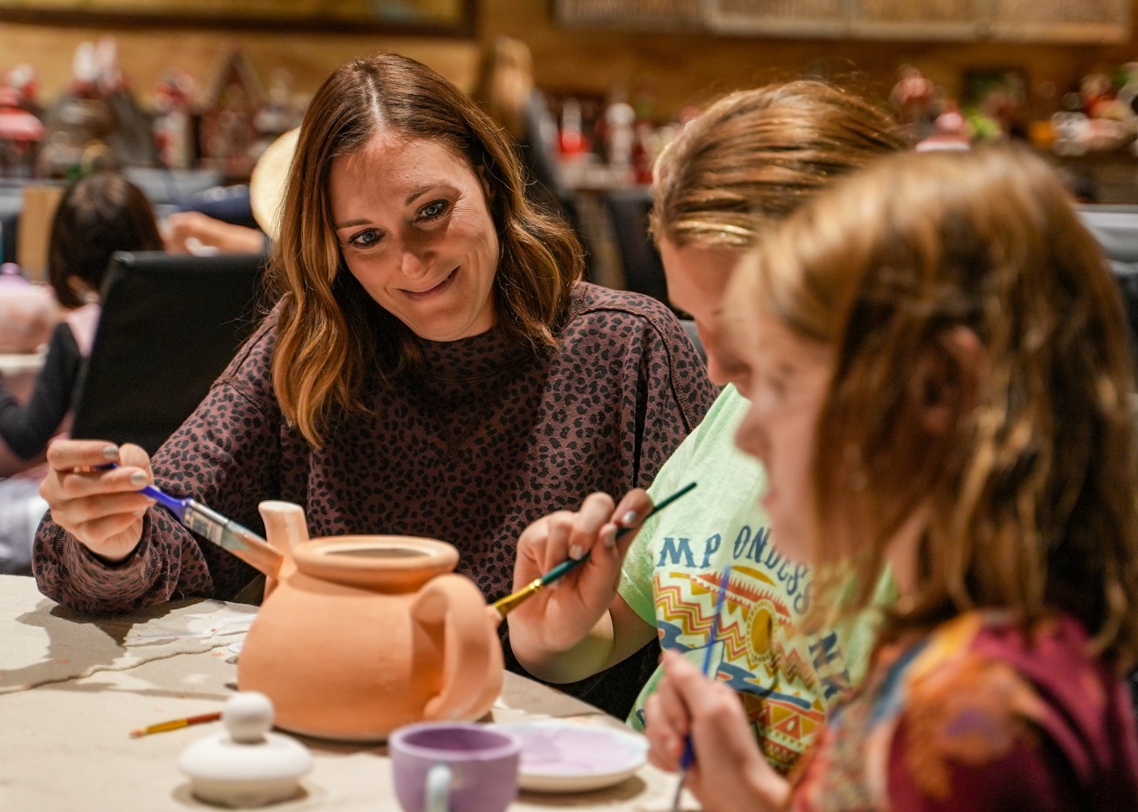 A mother and two daughters paint a ceramic teapot
