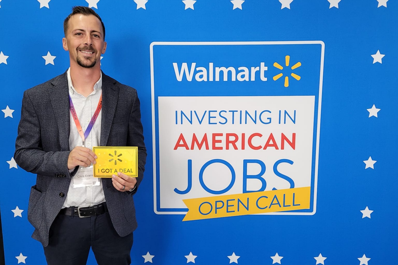 Chris Evans, of Evans Food Company, poses in front of a blue backdrop with the words "Walmart, Investing in American Jobs Open Call" printed on it