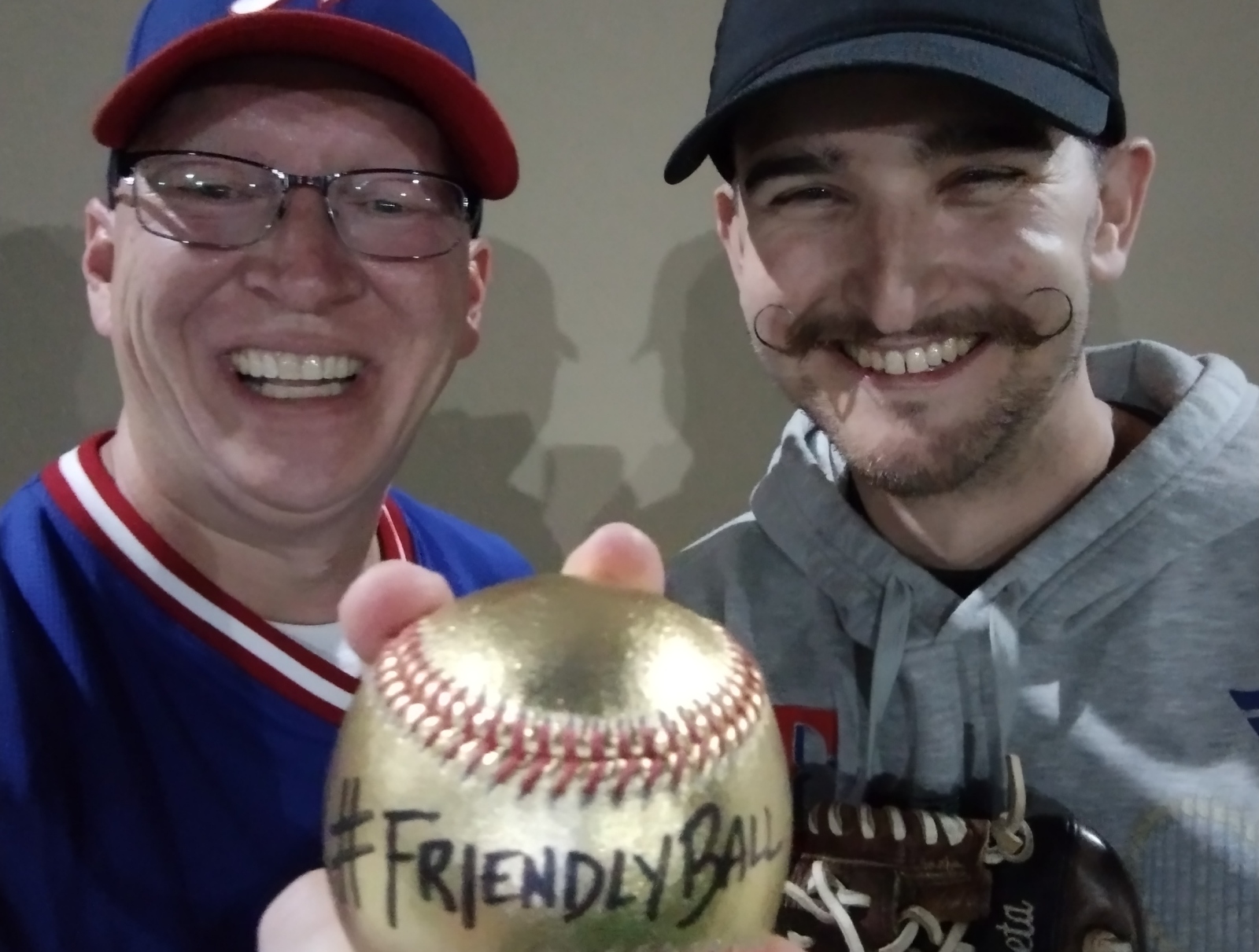 Ethan Bryan, left, and Mark Zubizarreta hold up a gold baseball labeled #FriendlyBall