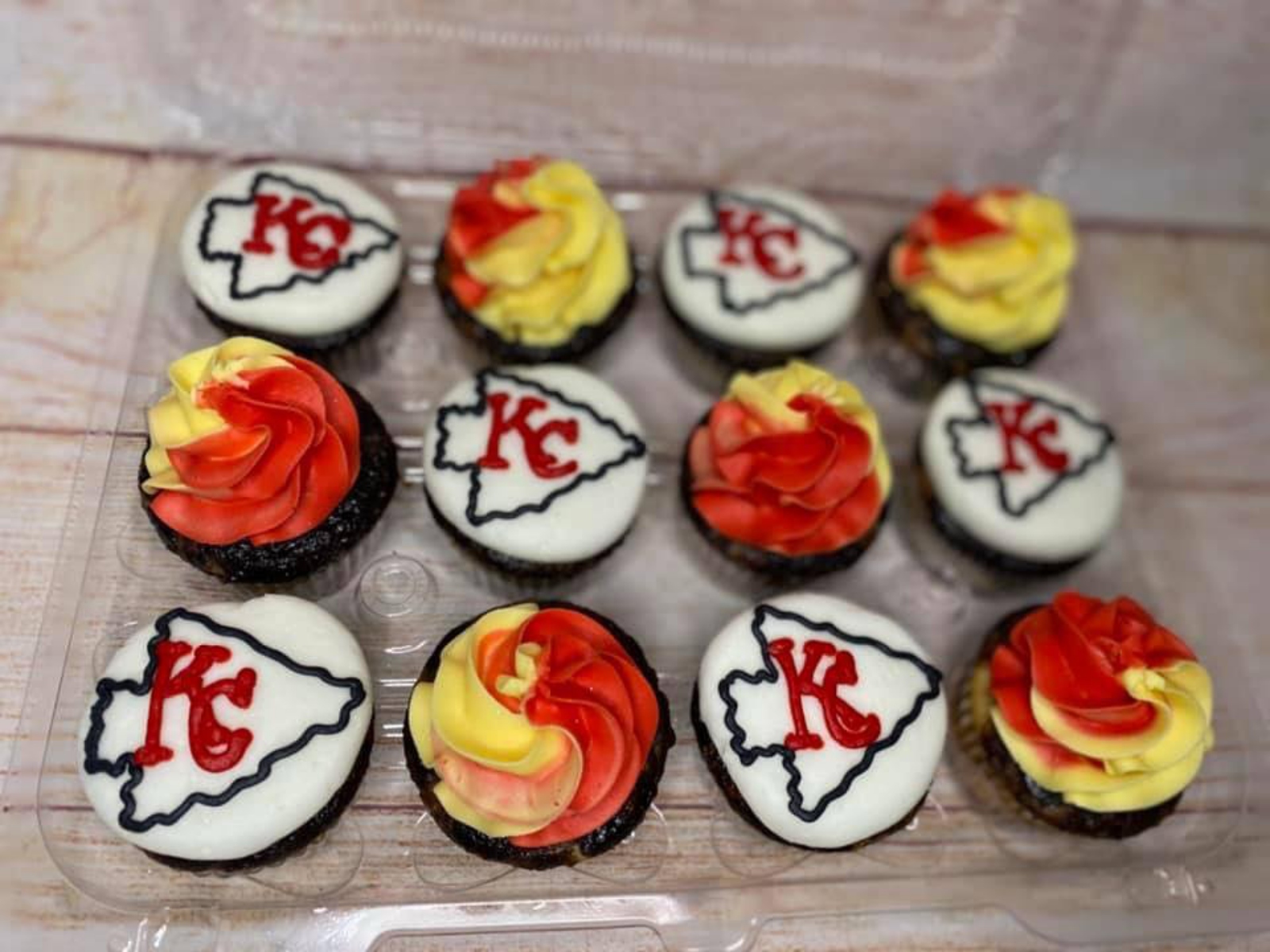 A tray of cupcakes decorated with Kansas City Chiefs logos and red and yellow frosting.