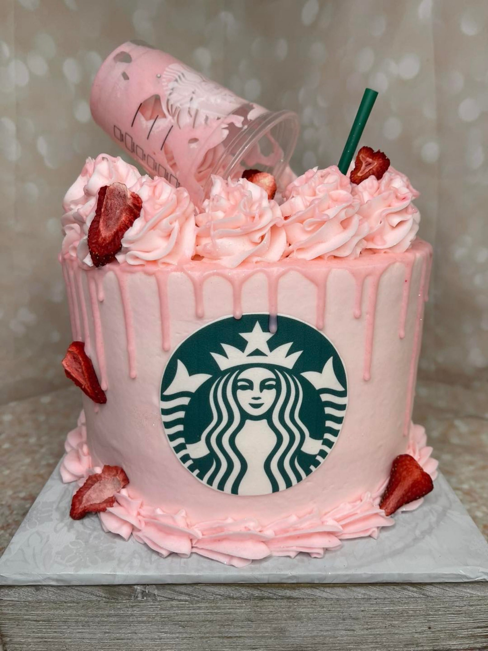 A pink cake decorated with a Starbucks logo and strawberries