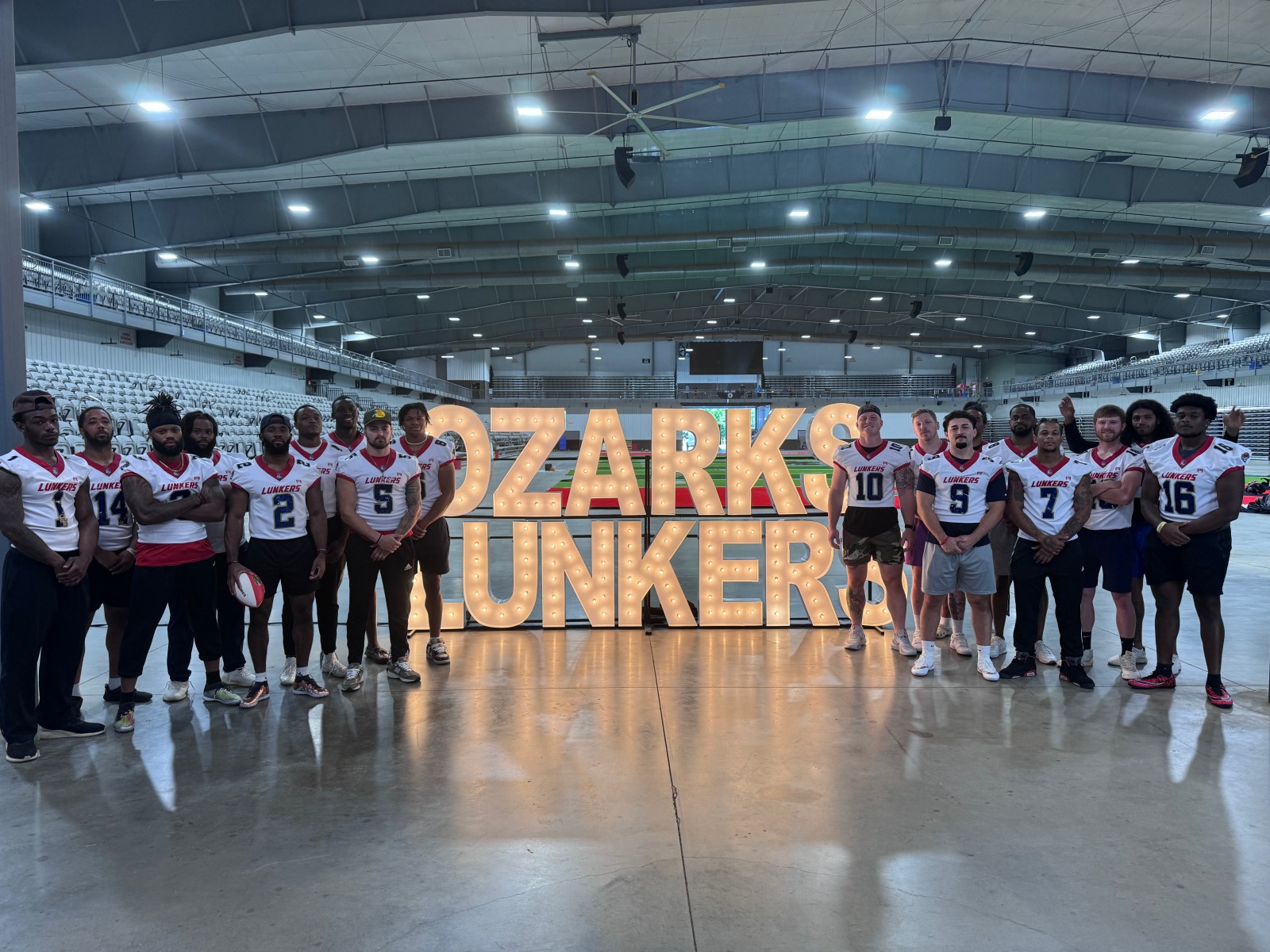 Players from the Arena League's Ozarks Lunkers pose for a photo next to giant light-up letters reading "Ozarks Lunkers."