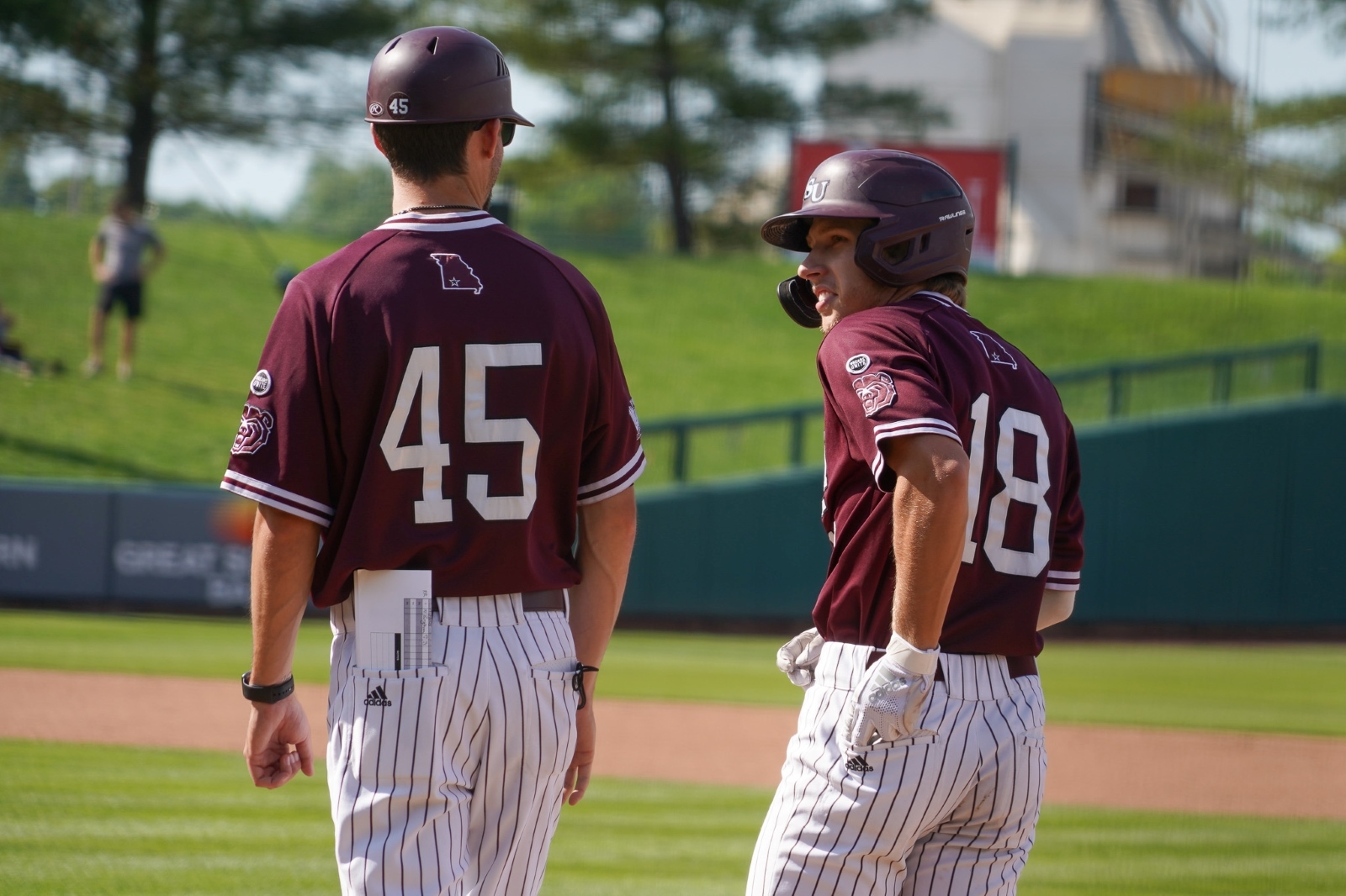 Spencer Nivens, wearing a Missouri State baseball uniform, stands on first base and talks to coach Jeremy Cologna