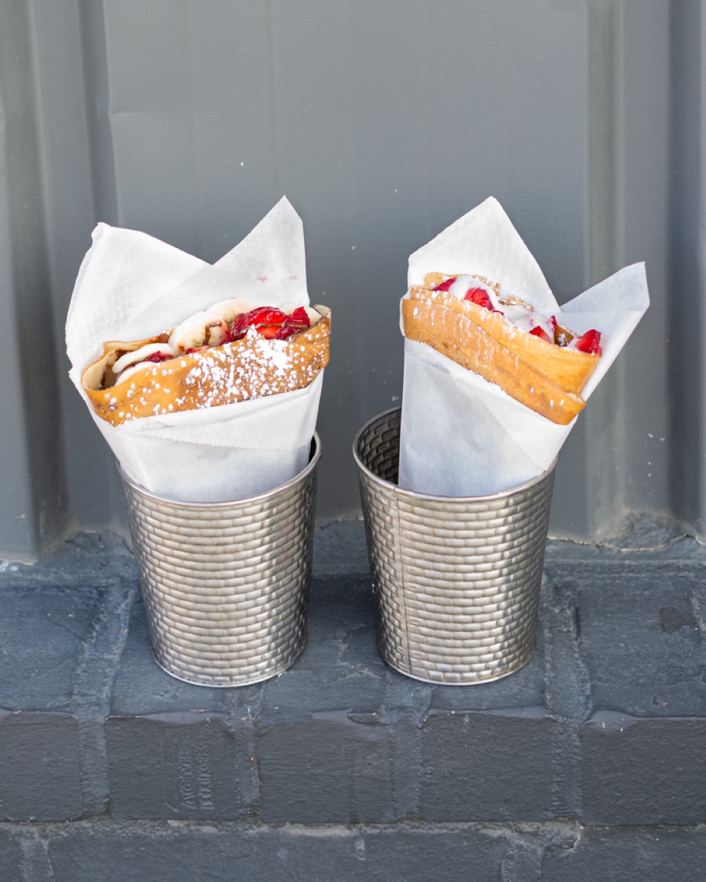 Crêpes wrapped in white deli paper sit in silver cans