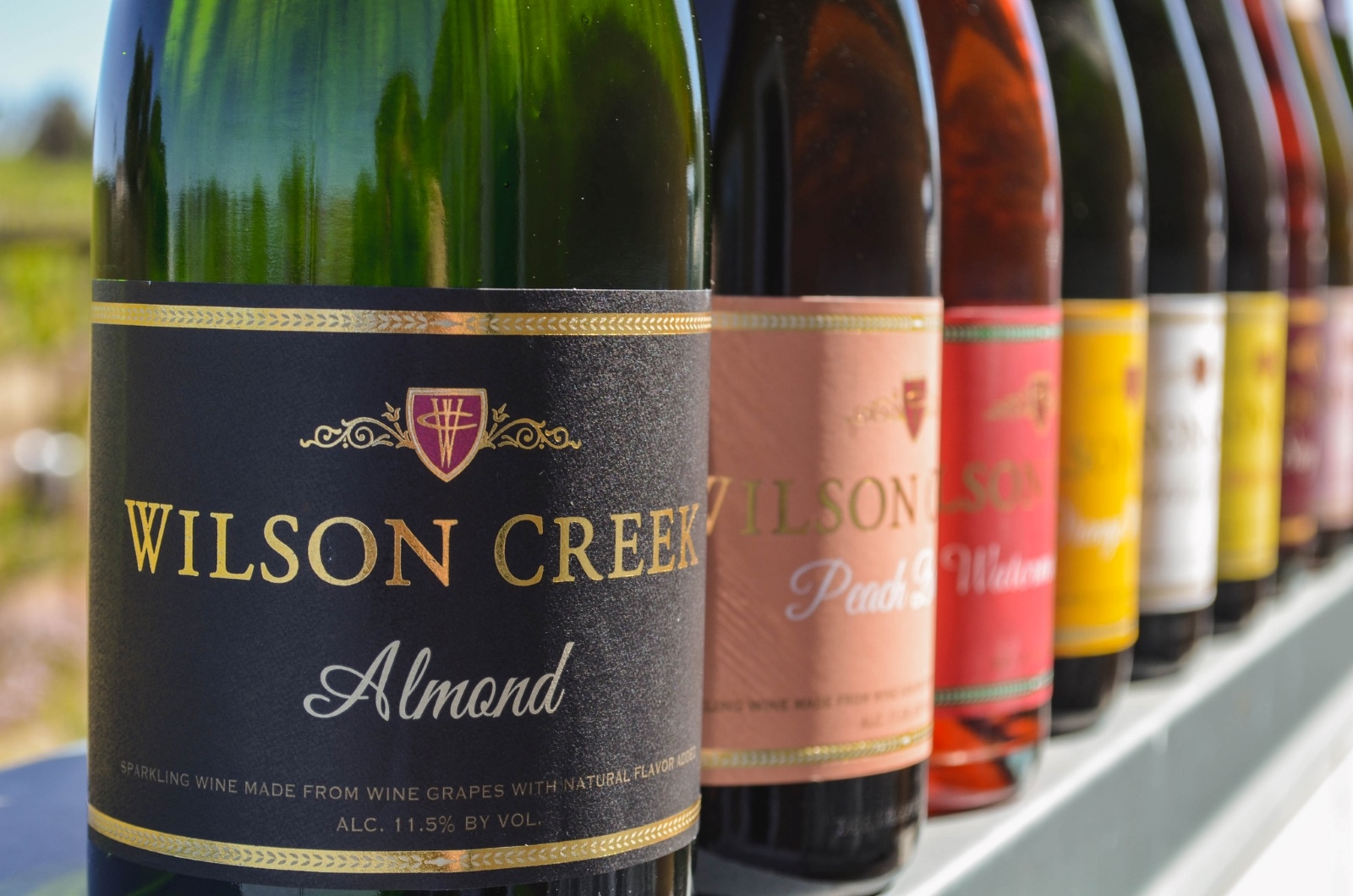 Bottles of Wilson's Creek Winery wines, with different colored labels, are lined up on a ledge.